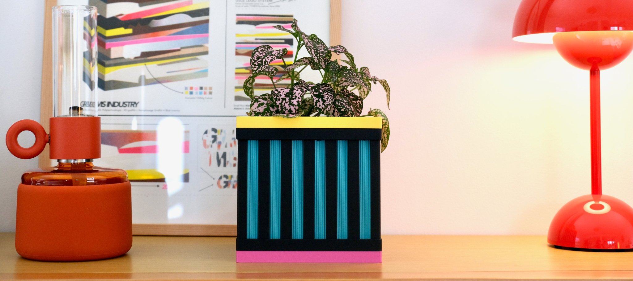 Le Cube N°1 noir et lagon posé sur une étagère, entre une lampe et un cadre