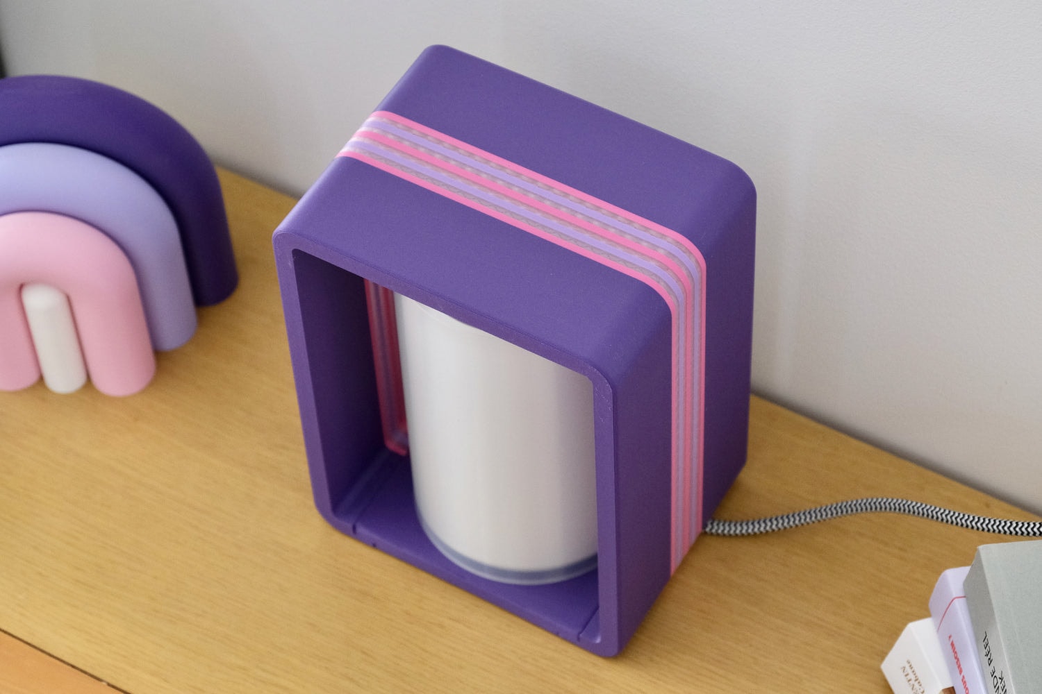 The Interstice lamp in purple on a wooden bedside table